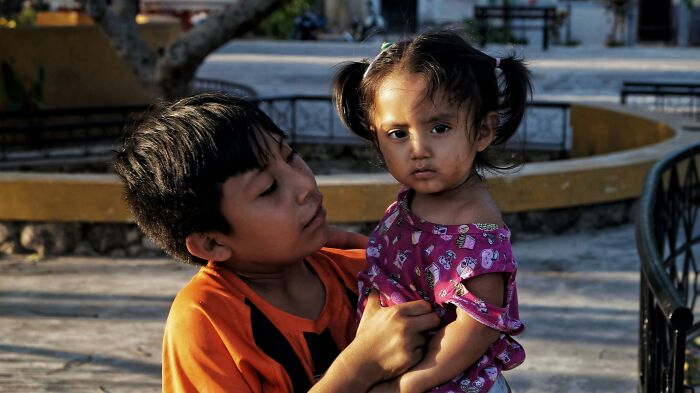 Young travelers experiencing culture shock, with an older boy holding a younger girl, both looking serious.