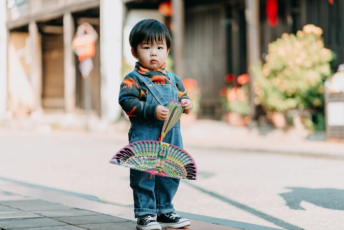 A young child, a traveler, holding a colorful fan on a street, potentially experiencing culture shock.
