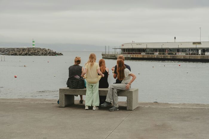 Travelers experiencing culture shock while sitting by the harbor with a lighthouse and buildings in the background.