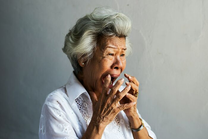 An elderly woman looks shocked, clutching her face, illustrating unusual ways people have lost their lives.