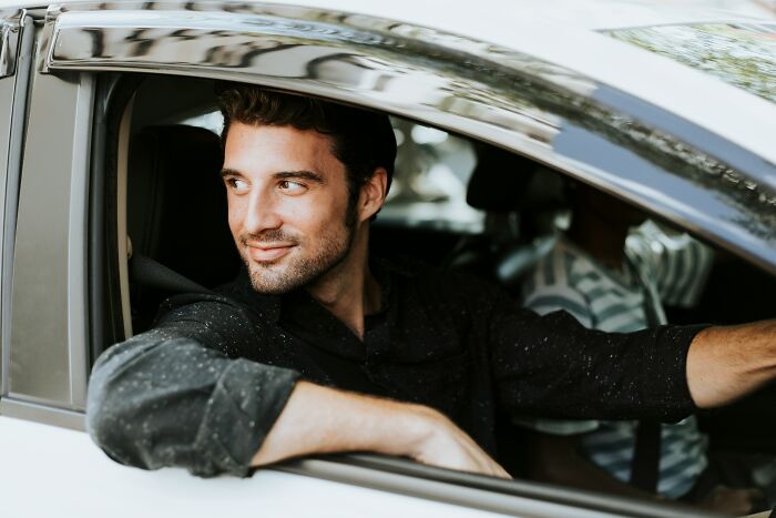 A man in a car, looking out the window with a confident smile, perhaps avoiding an instant justice moment.