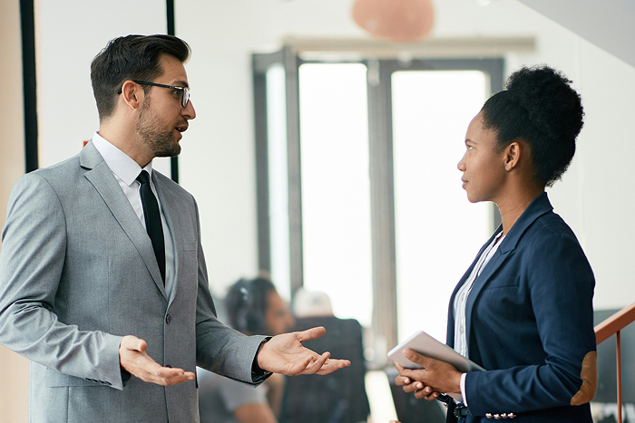 A man mansplaining to a woman in a business setting, who listens intently, highlighting infuriating mansplaining.