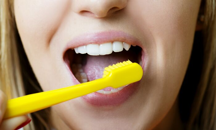 A close-up of a person brushing their teeth with a bright yellow toothbrush, revealing clean white teeth. This image highlights facts people wish they could forget.