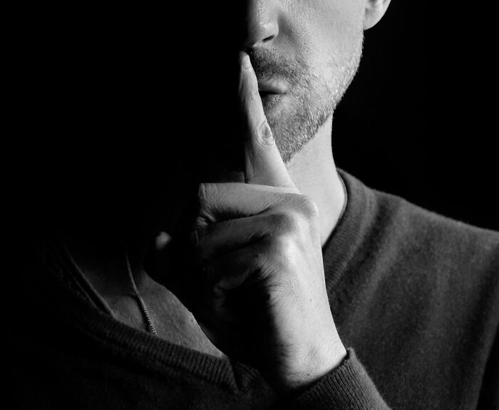 A man with his finger on his lips, signifying secrets or facts people wish to forget.