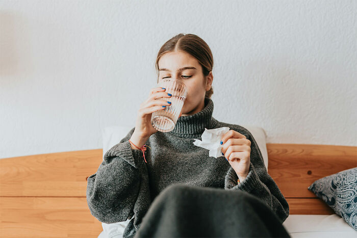 A young woman in bed, drinking water and holding a tissue, wanting to forget facts.