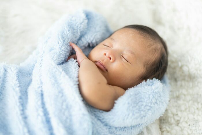 A newborn baby wrapped in a blue blanket, too young to learn facts people wish to forget.