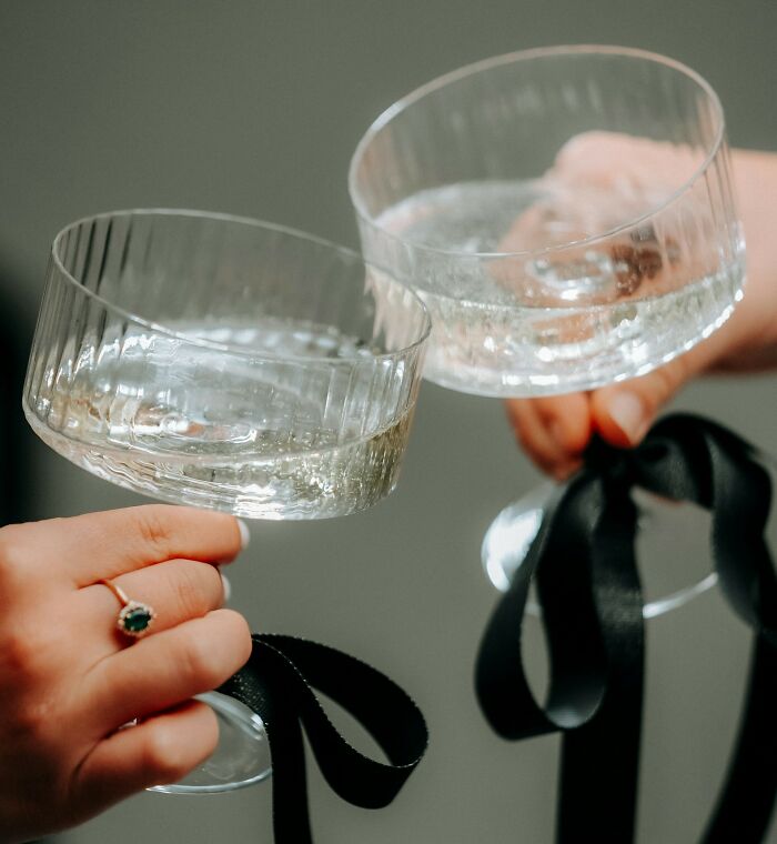 Two hands clinking glasses of champagne, wishing they could forget some facts.