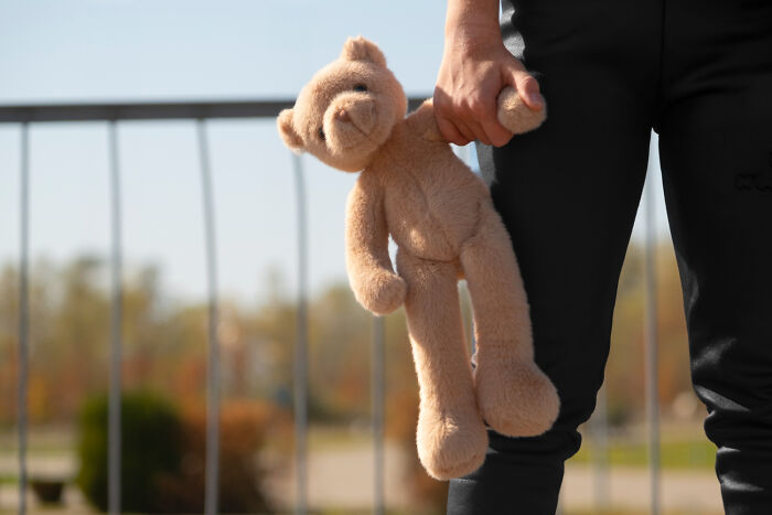 A person holding a brown teddy bear by its arm outdoors, a familiar sight for uncovering forgotten facts.