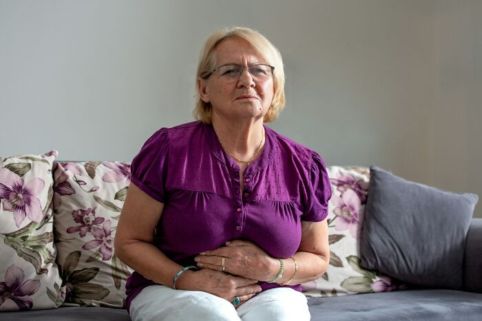 An elderly woman holding her stomach in pain, showing facts people wish to forget due to discomfort.
