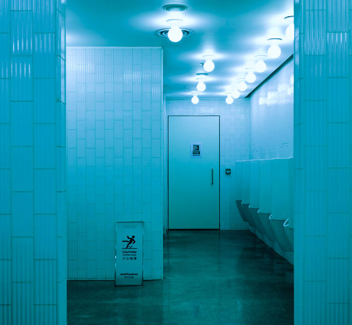 A stark blue-lit public restroom with urinals and a closed door, representing unsettling facts people wish they could forget.