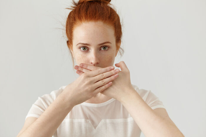 A redhead woman covering her mouth, expressing a desire to forget facts she learned.