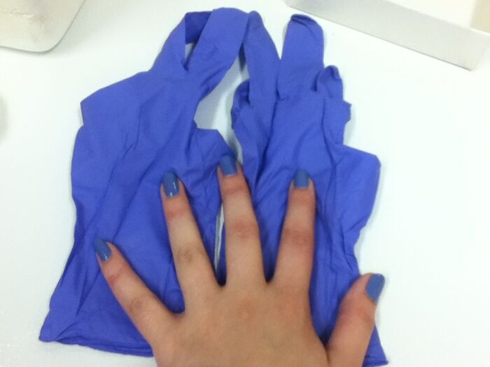 A hand with purple nail polish perfectly matching a pair of purple medical gloves, demonstrating satisfying paint matches.
