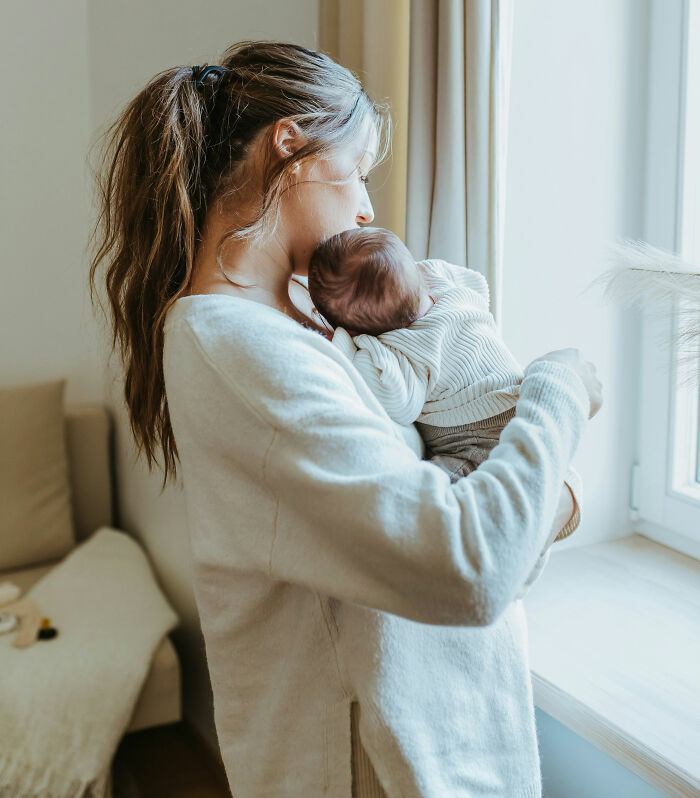 A mother gently holds her baby, possibly musing over infuriating stories about MILs.