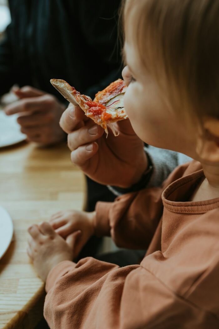 A child eating a slice of pizza, a common public scene, but could hide disturbing details.