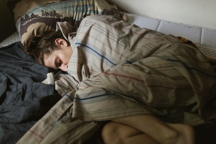 A person sleeping in bed, covered by a striped blanket. This image reflects unhinged therapist moments.