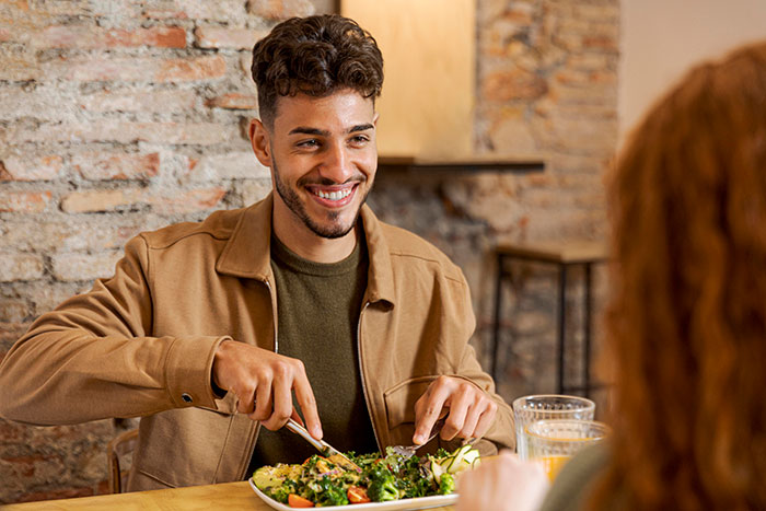 A happy boyfriend enjoying a dinner table habit of eating a salad with chopsticks, defending his bizarre behavior. A happy boyfriend enjoying a dinner table habit of eating a salad with chopsticks, defending his bizarre behavior.