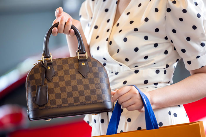 A woman holds a luxury designer purse with a checked pattern, illustrating the value of the slashed designer purse. A woman holds a luxury designer purse with a checked pattern, illustrating the value of the slashed designer purse.