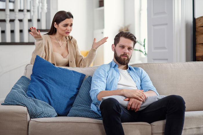 A woman expressing frustration at a man sitting on a couch, related to a jealous stepsister. A woman expressing frustration at a man sitting on a couch, related to a jealous stepsister.
