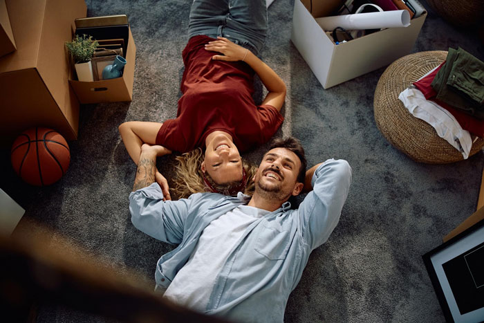 A couple lying on the floor, surrounded by boxes, symbolizing issues like a husband's plan to charge rent to a daughter's boyfriend. A couple lying on the floor, surrounded by boxes, symbolizing issues like a husband's plan to charge rent to a daughter's boyfriend.