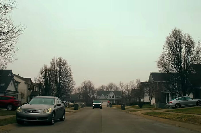 A quiet suburban street with houses and cars, setting the scene for a worst neighbor ever incident.