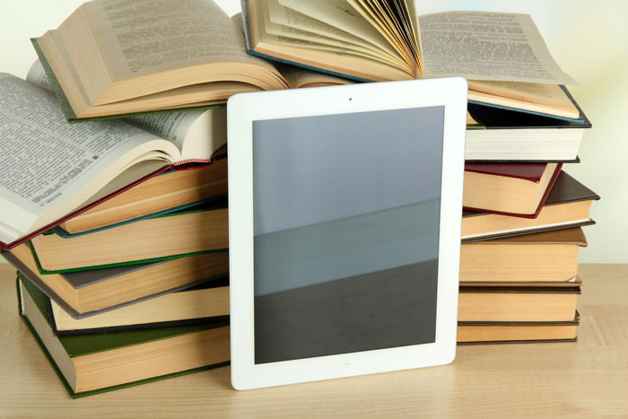 A white tablet, possibly a Kindle, stands upright against a stack of physical books, symbolizing the Kindle she regrets giving away. A white tablet, possibly a Kindle, stands upright against a stack of physical books, symbolizing the Kindle she regrets giving away.