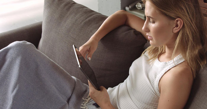 A woman on a couch looking at her Kindle, after giving it away and regretting it after a decade. A woman on a couch looking at her Kindle, after giving it away and regretting it after a decade.