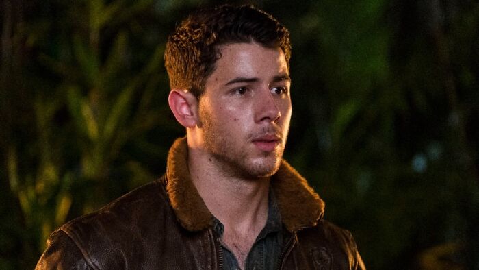 Nick Jonas in a brown leather jacket, looking off to the side, portraying a disillusioned celebrity.