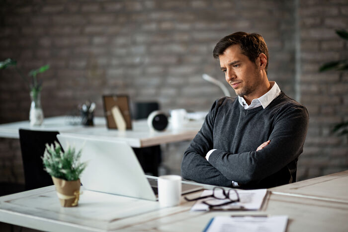A thoughtful male worker looking at his laptop, contemplating corporate buzzwords and practices.