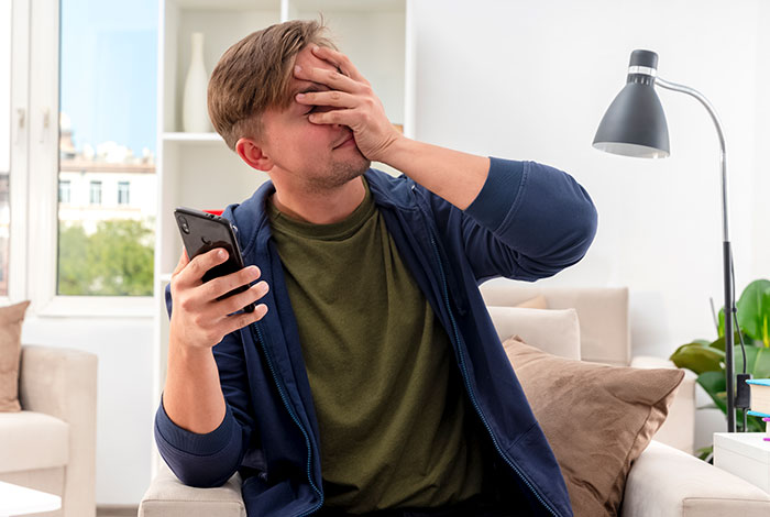 A man covers his face, looking distressed while holding a phone, symbolizing the family feud over a childfree wedding. A man covers his face, looking distressed while holding a phone, symbolizing the family feud over a childfree wedding.