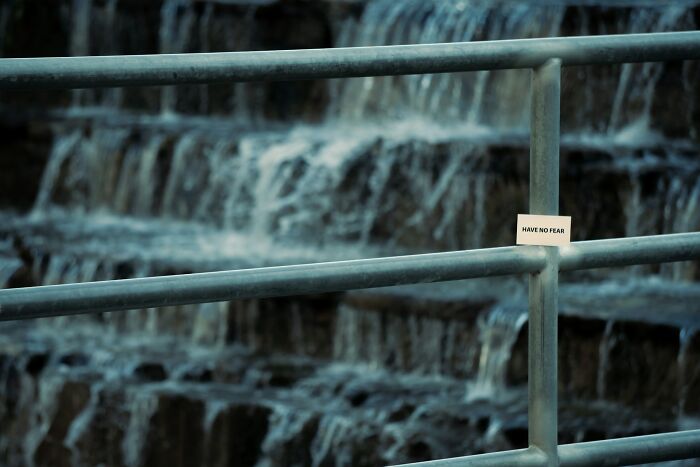 A sign on a railing saying 'Have No Fear' by a waterfall, an oddly comforting public sight.
