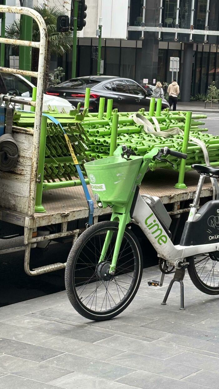 A Lime e-bike parked next to a truck carrying green construction scaffolding, an incredibly satisfying paint match.