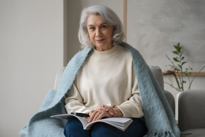 An elderly woman wrapped in a blanket, reading a book, contrasting with gross stories about guests.