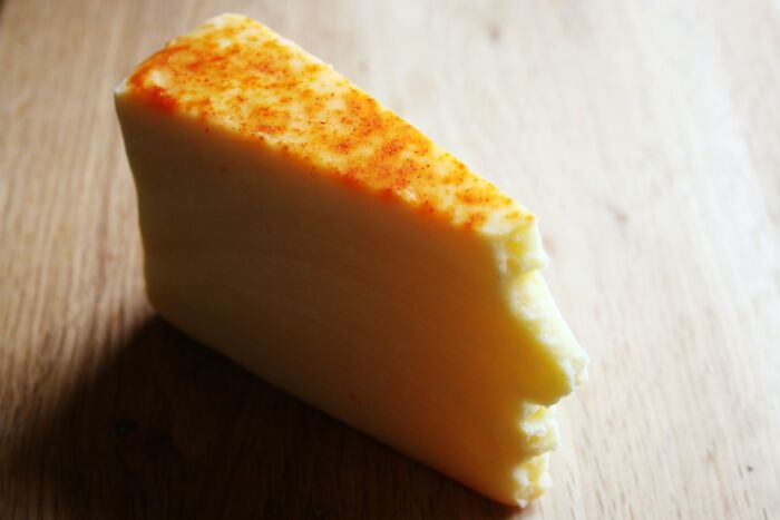 A wedge of cheese on a wooden surface, with red seasoning, that resembles an ugly human profile, a public horror story.