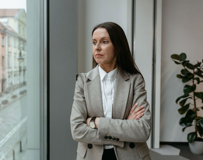 A woman in a grey blazer with arms crossed, looking out a window, representing an entitled aunt. A woman in a grey blazer with arms crossed, looking out a window, representing an entitled aunt.
