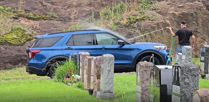 A man washing his blue car in a cemetery, surrounded by tombstones, showing people who think they are the main character.