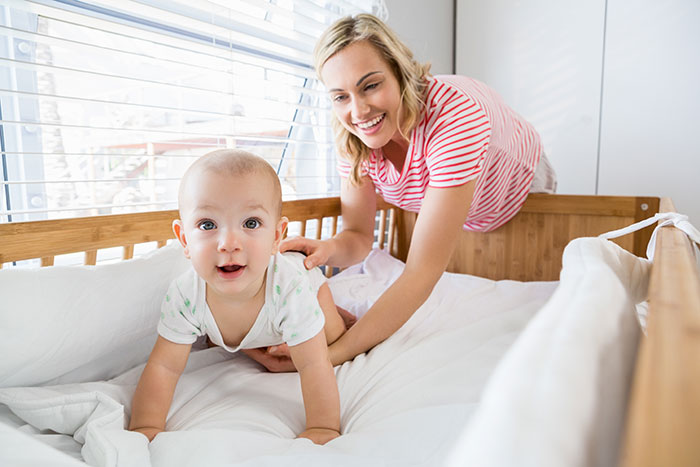 A smiling mom and a happy baby in a crib. The mom reminds the nanny of her employer role and boundaries.
