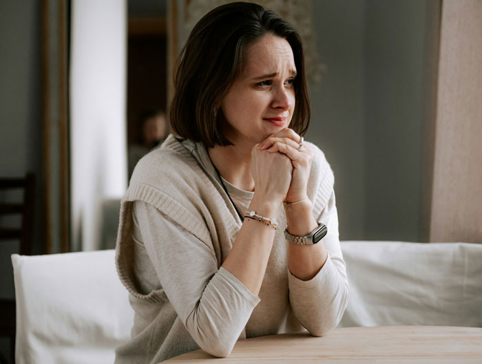 A woman looking distraught, hands clasped, expressing emotion in the great-grandma's trolling story. A woman looking distraught, hands clasped, expressing emotion in the great-grandma's trolling story.