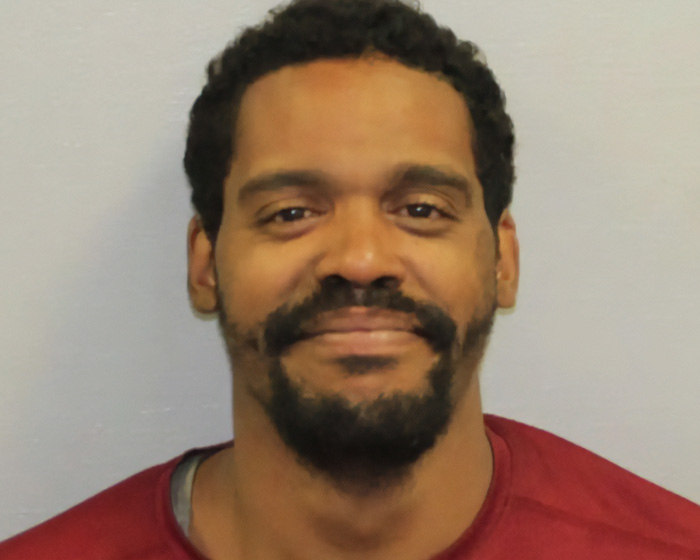 Mugshot of a smiling man with a beard and curly hair, involved in stupid arrests.
