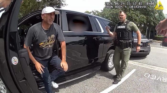 A man in a white hat being stopped by a sheriff officer next to a black SUV, leading to stupid arrests.