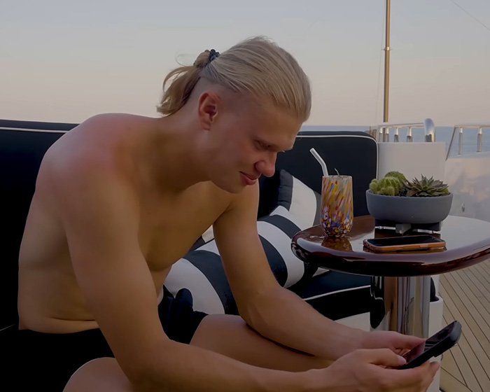 Erling Haaland on a yacht, checking his phone, reacting to internet memes about himself.