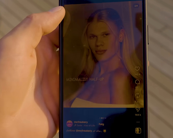 A hand holds a phone displaying an image of Erling Haaland in a minimalist half-up hairstyle from an internet meme.