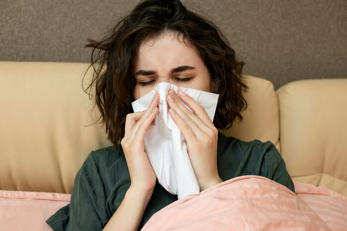A woman blowing her nose with a tissue, an everyday item people use for different things.