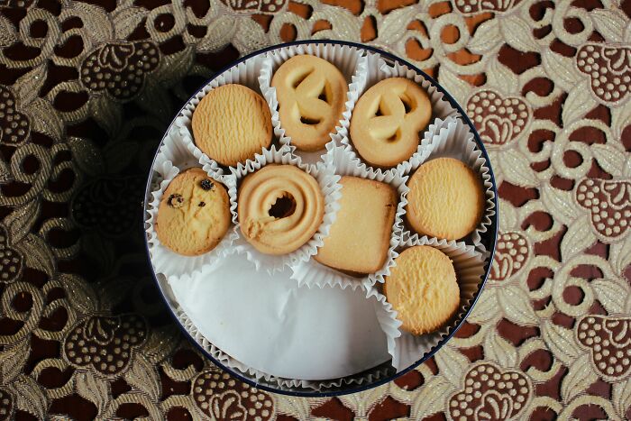 An open tin of assorted cookies on a patterned tablecloth, representing everyday items for different things.