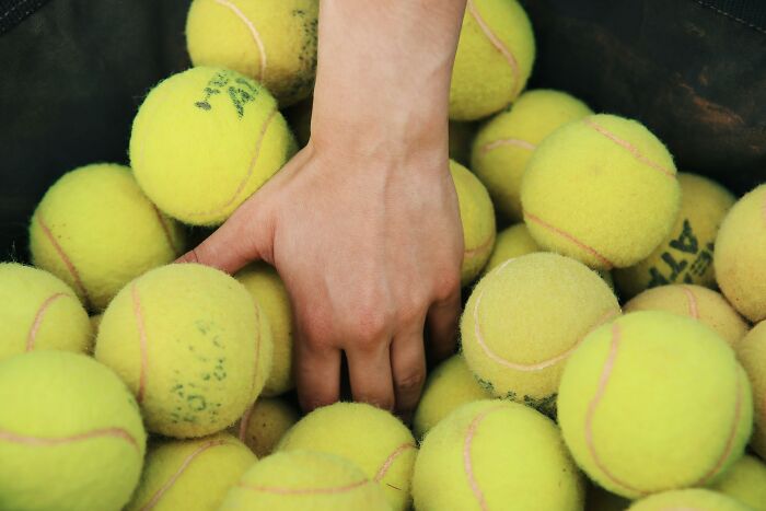 A hand reaching into a pile of tennis balls, illustrating everyday items with surprising alternative uses.