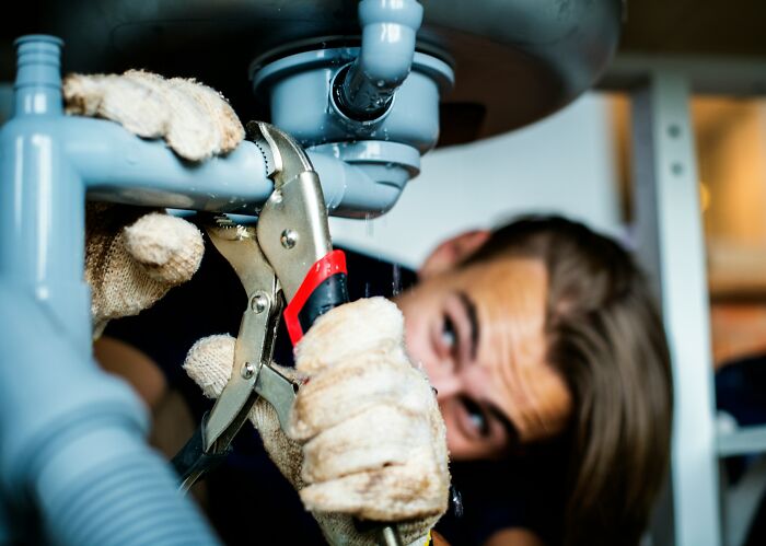 A plumber fixing a leaky pipe under a sink, demonstrating everyday items with different uses.
