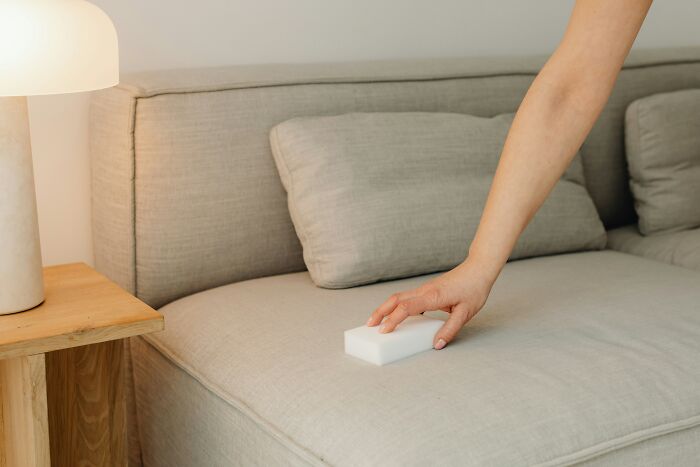 A hand cleaning a sofa with an everyday item, a magic eraser, used for completely different things.