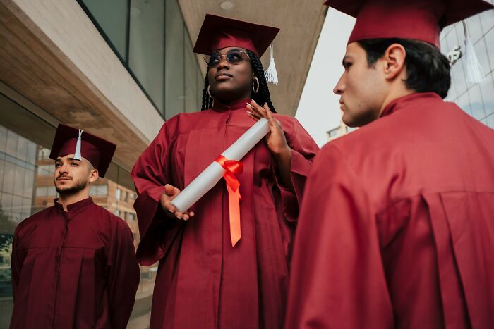 Graduates in red caps and gowns, one holding a diploma, demonstrating everyday items for different uses.