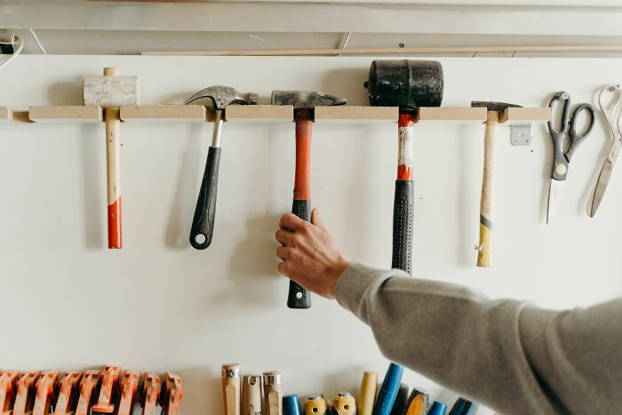 Hand reaching for a hammer hanging on a wall, an everyday item secretly used for different things.