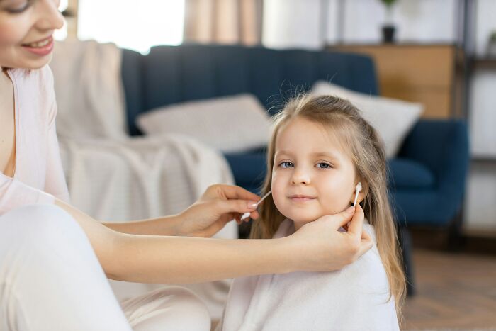 A woman helping a young girl with earbuds, demonstrating everyday items for unexpected uses.
