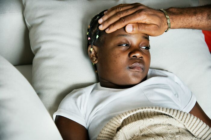 A person checking the forehead of a child lying on a couch, illustrating everyday items.
